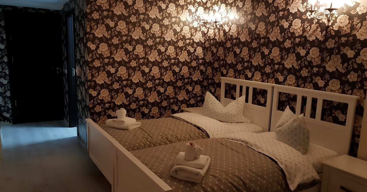 Cameră cu două paturi single și tapet floral decorativ